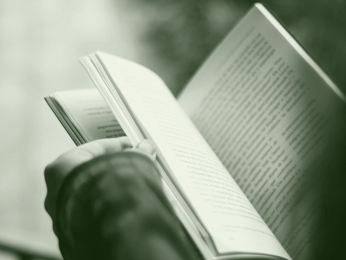 Une main tient un manuel ouvert, le pouce pose sur la tranche des pages, le texte imprime s'etendant sur les deux feuillets dans une lumiere douce.