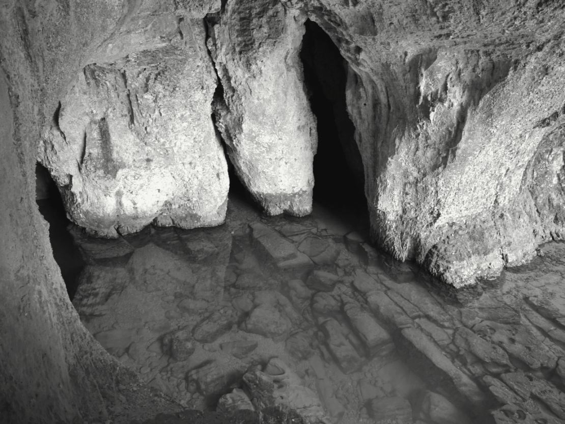 Sous une voûte de calcaire, une eau très claire remplit le fond d'une grotte et s'écoule vers l'extérieur entre des blocs de rocher : c'est de là que sort la rivière.