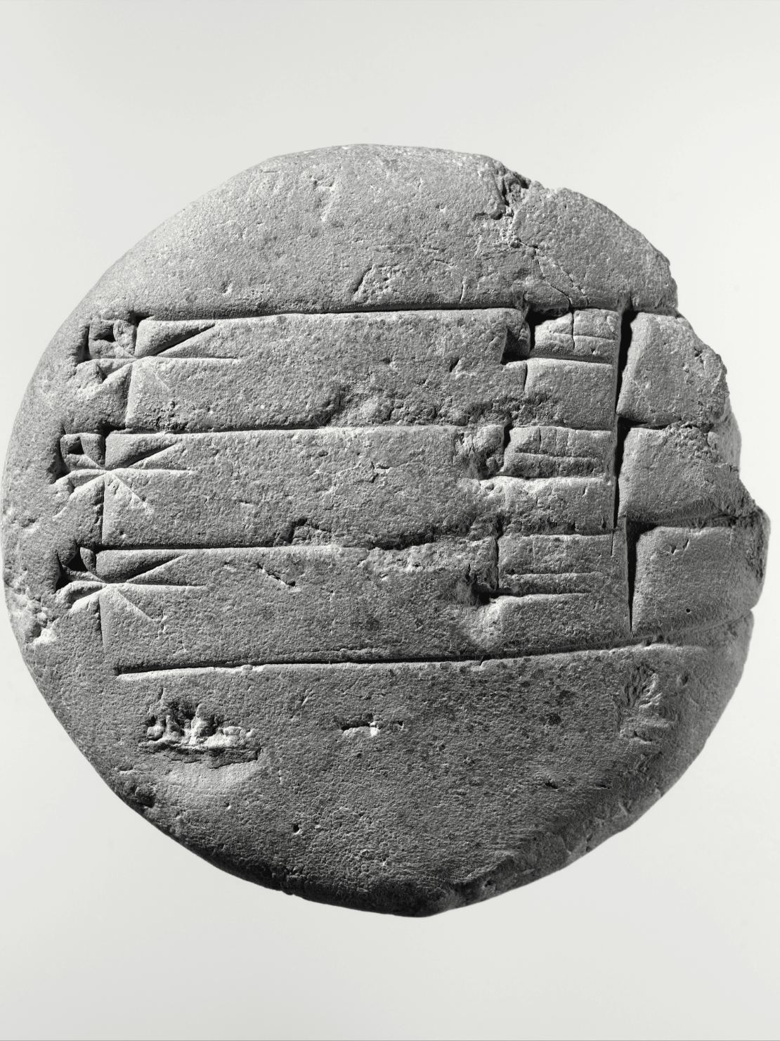 Une tablette d'argile ronde, de la taille d'une paume, couverte de signes en forme de coins tracés en lignes horizontales séparées par des traits.