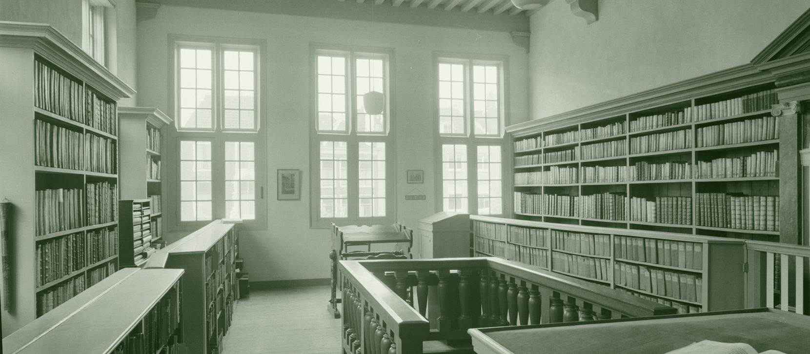 Une salle de lecture ancienne, photographiée sans personne : des rayonnages de volumes en vélin couvrent les murs, un grand livre est ouvert sur un lutrin au premier plan.