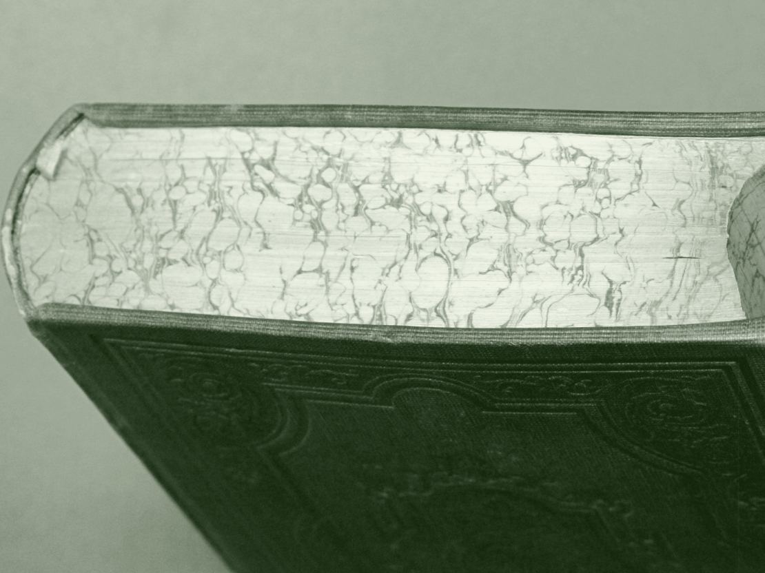 La tranche marbrée d'un livre du dix-neuvième siècle, vue de dessus : des veines irrégulières courent sur le papier, et le plat de toile gaufré apparaît en dessous.